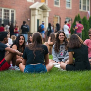 group of students sitting on the grass in a circle in front of a brick building
